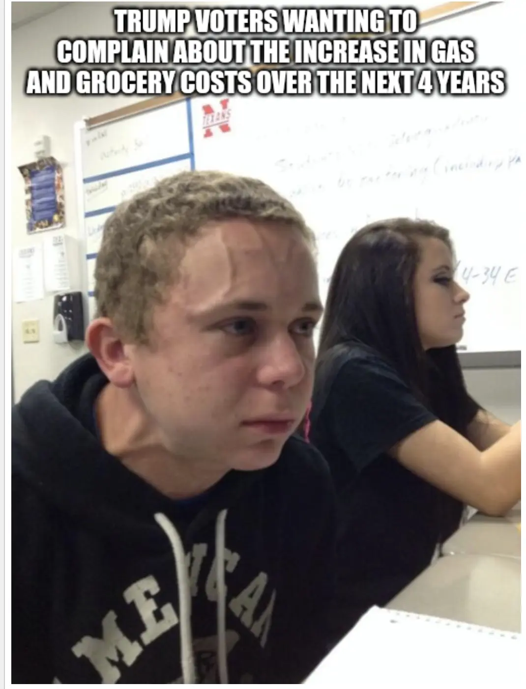 A photo of a young man in a classroom wearing a black hoodie with 'AMERICAN' visible, looking visibly distressed with…