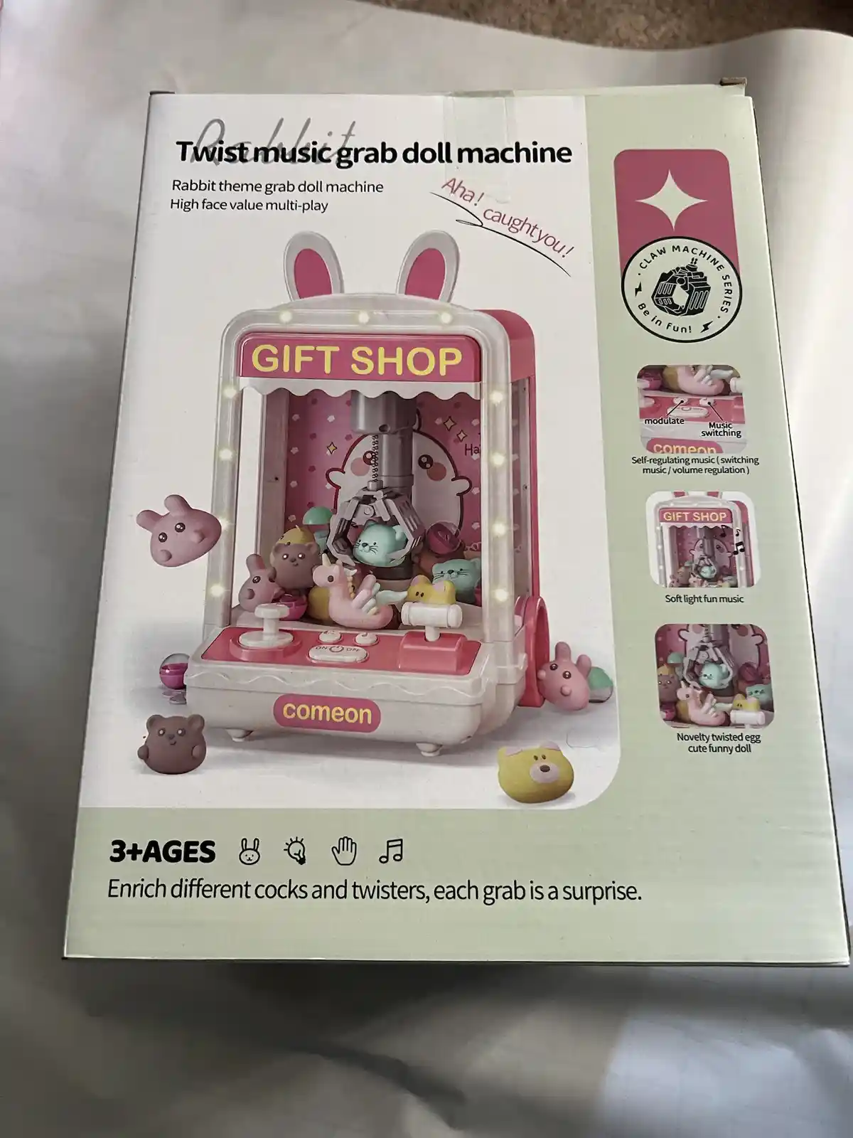 The image shows a product box for a 'Rabbit theme grab doll machine' with a pink and white claw machine design featuring…