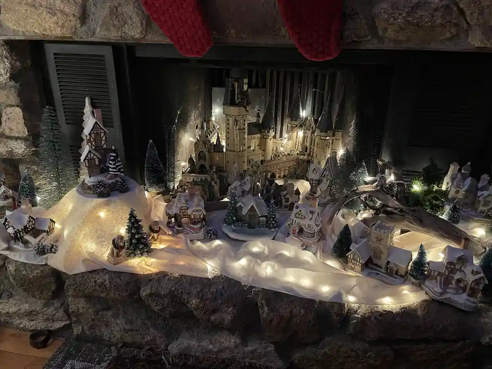 A festive miniature winter village diorama is displayed inside a stone fireplace, featuring a large illuminated Harry Potter…