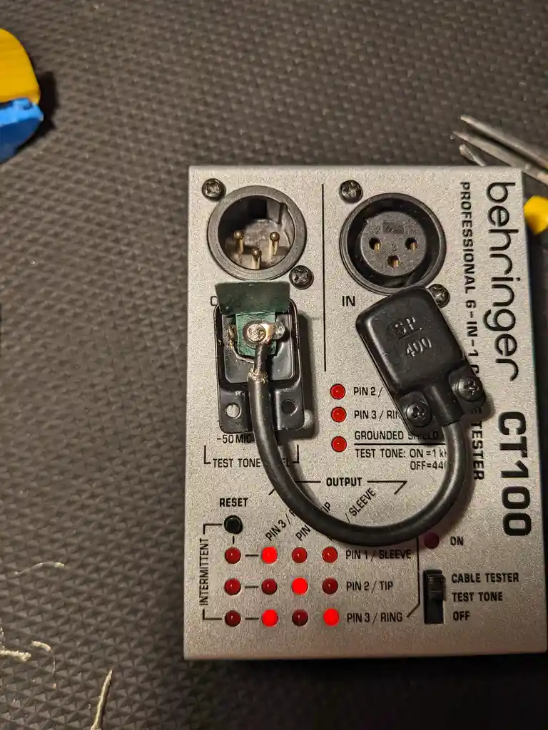 A Behringer CT100 professional 6-in-1 cable tester with all its red indicator lights illuminated, showing a cable is fully…