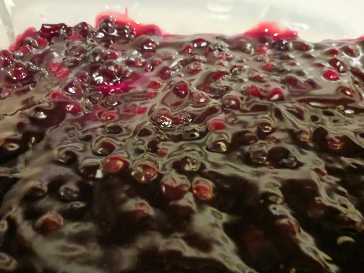 A close-up photo shows a thick, dark purple berry mixture with whole and crushed berries suspended in a glossy, bubbling…
