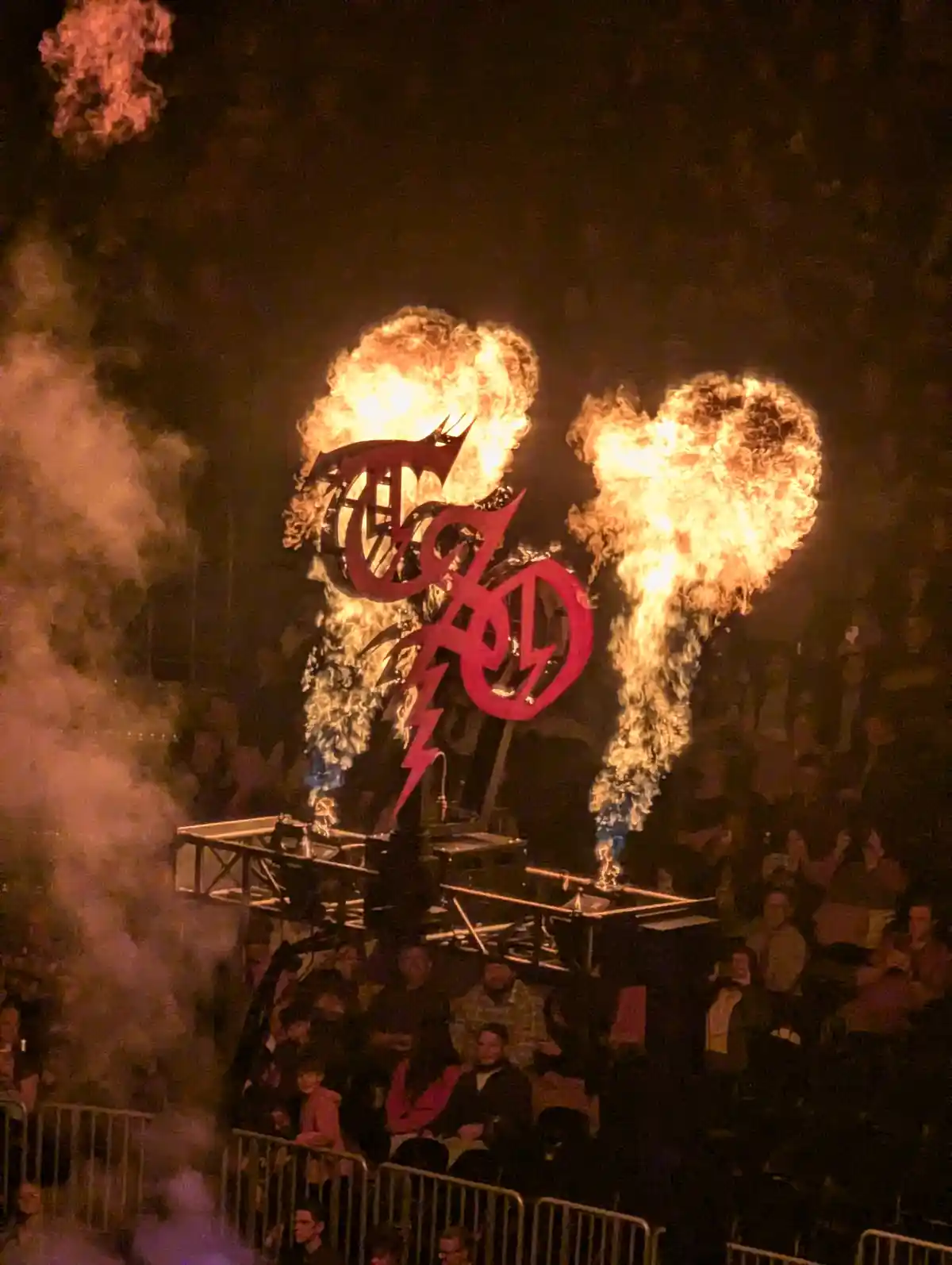 A fiery stage display at a concert features a large red metal sign with the band name 'taylor swift' in stylized lettering…