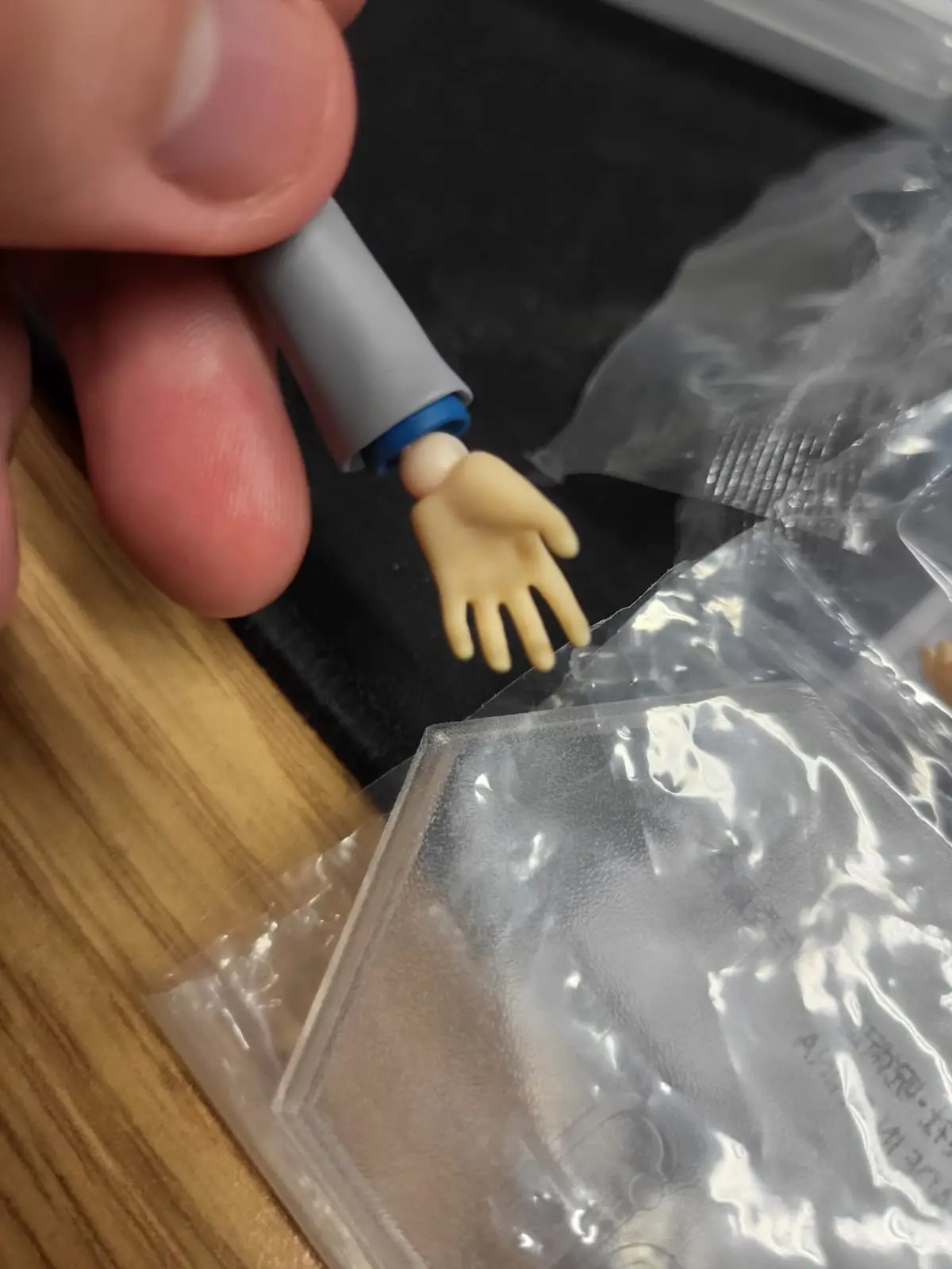 A close-up photo shows a person's thumb and forefinger holding a small, beige plastic action figure hand attached to a gray…