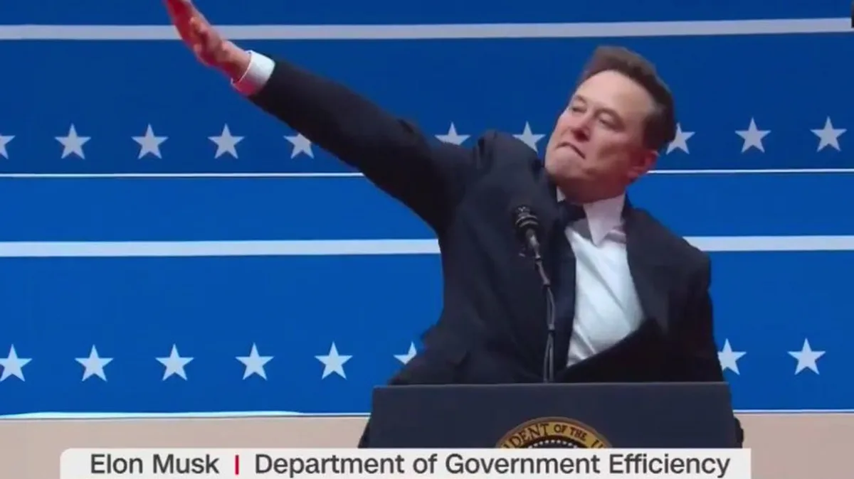 A man in a dark suit stands at a podium with a presidential seal, raising his right arm in a gesture resembling a political…