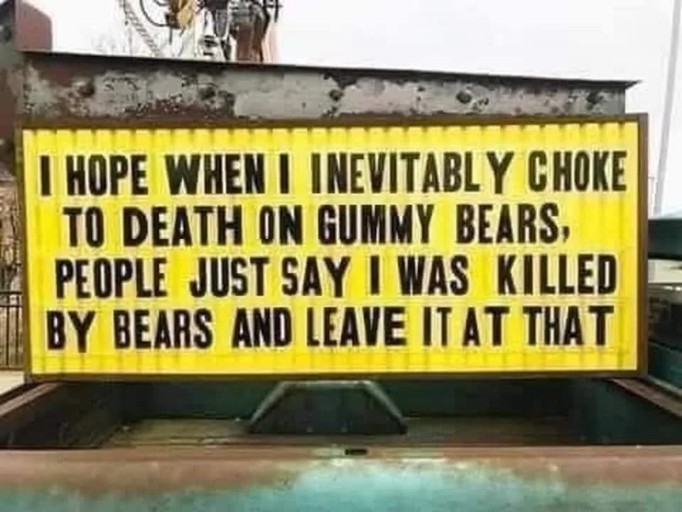 A yellow marquee sign with black lettering is mounted on a rusty metal structure, displaying a humorous message about dying…