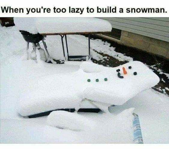 A snow-covered outdoor recliner chair has been shaped into a snowman, with small green buttons and a carrot nose, sitting in…