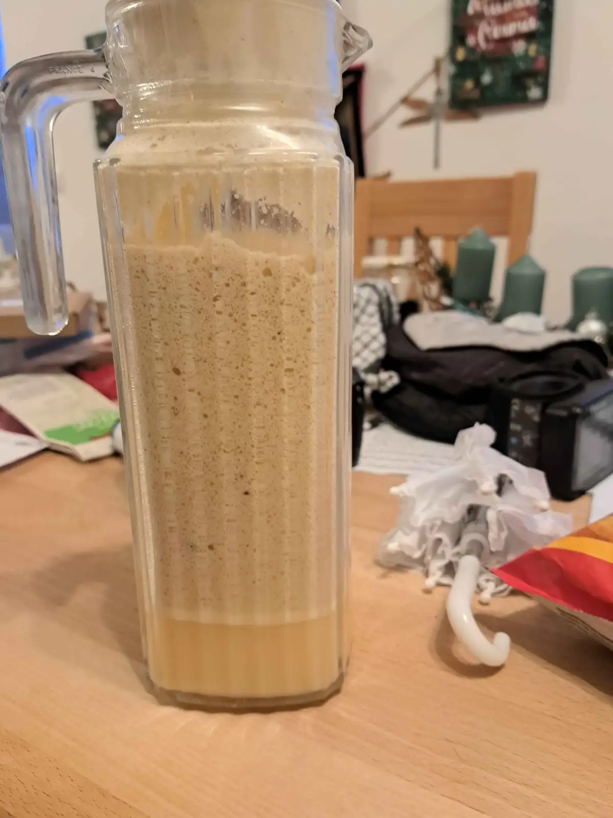 A clear glass pitcher filled with a light brown liquid that has a thick, bubbly foam layer rising up its sides, sitting on a…
