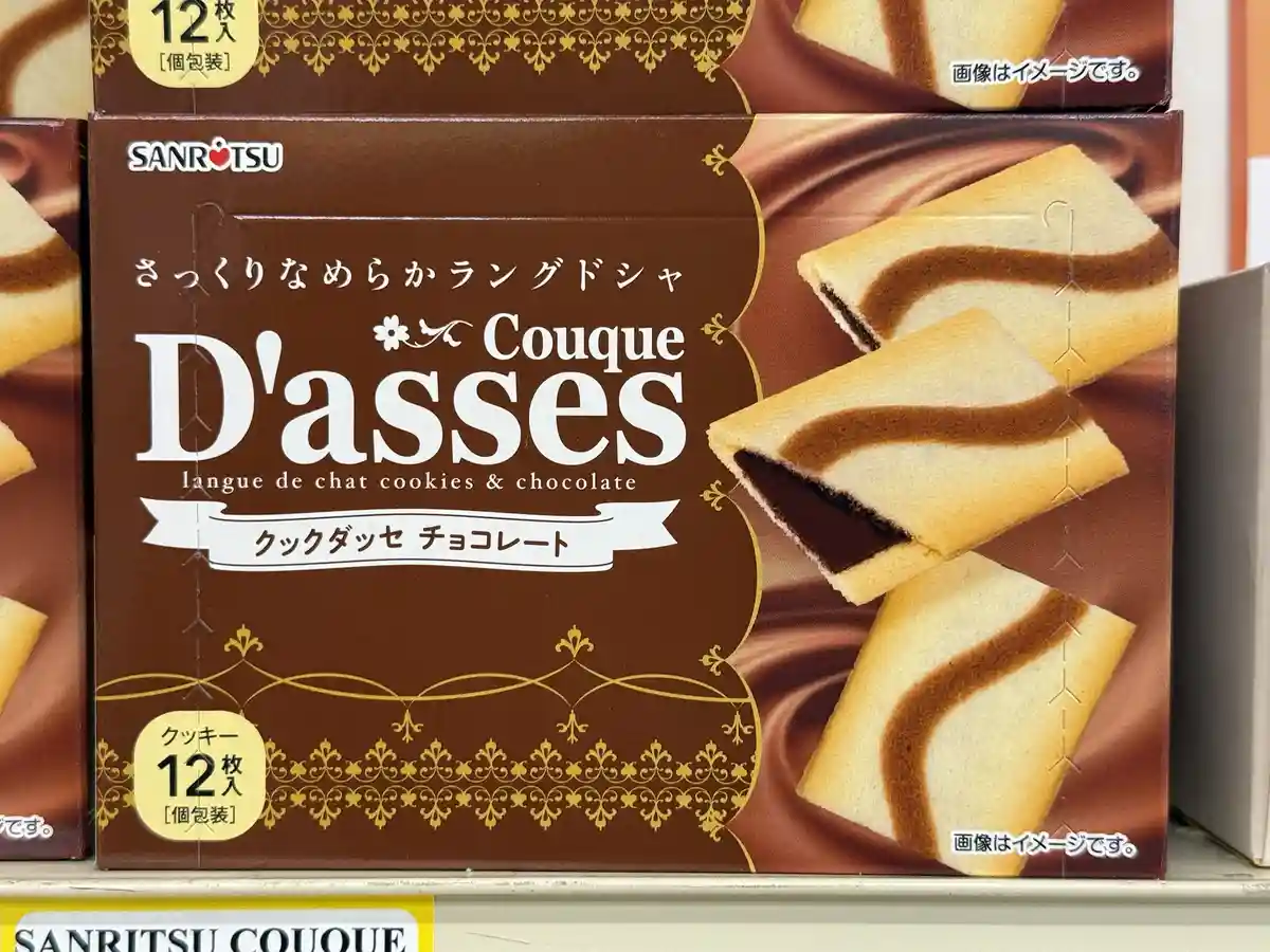 A close-up of a brown Japanese snack box for 'Couque D'asses' cookies, featuring a French phrase 'langue de chat' (cat's…