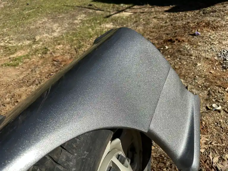 A close-up photo shows a car's fender painted in a glittery, sparkly silver finish, set against a backdrop of dirt and…