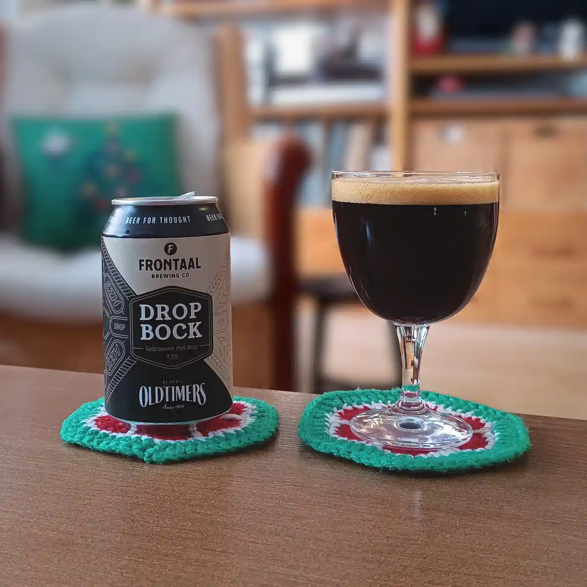 A can of Frontaal Brewing Co.'s 'Drop Bock' beer sits next to a glass of dark beer on a wooden table, both resting on…
