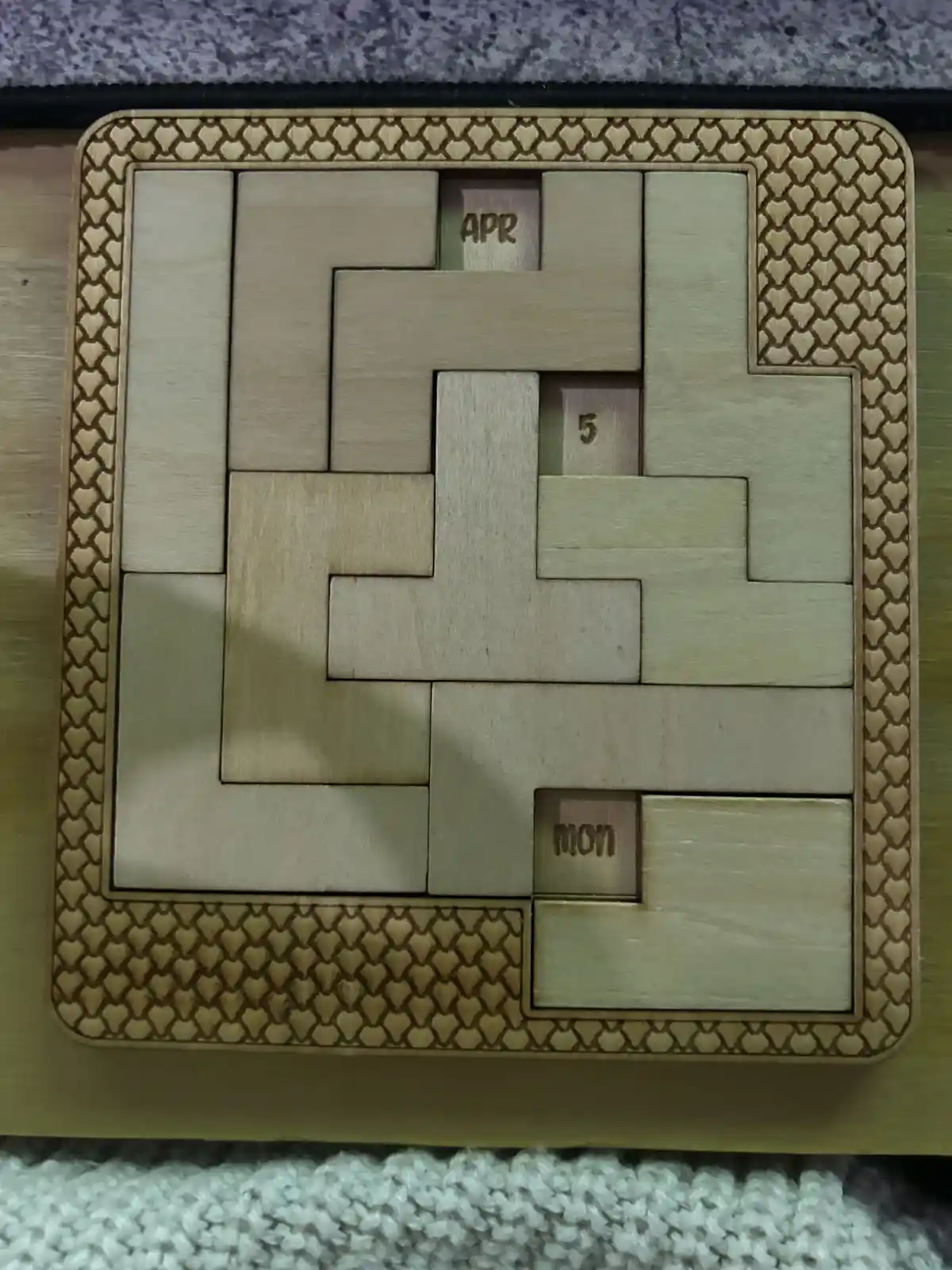 A wooden puzzle calendar with interlocking pieces, where three small blocks are visible: one labeled 'APR', one labeled '5'…