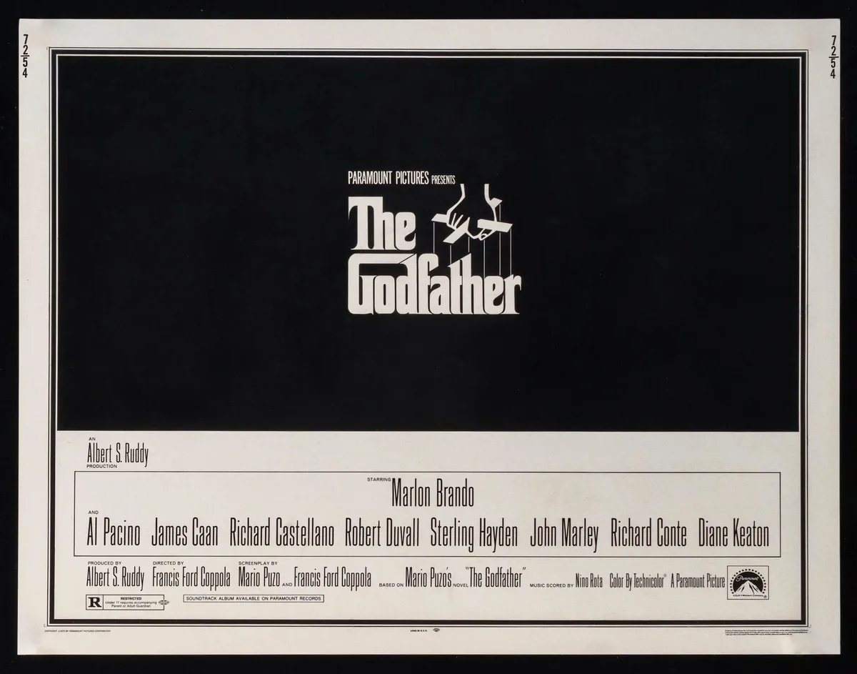 A black-and-white movie poster for 'The Godfather' shows the title in large white letters with a hand puppet motif…