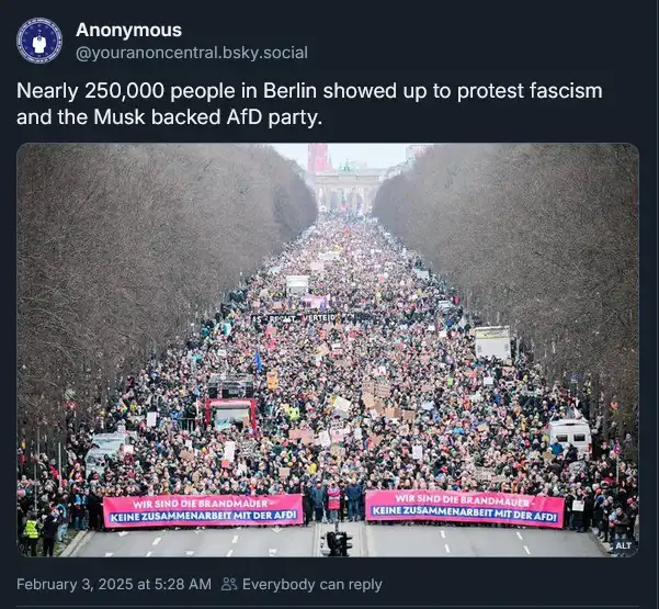 A wide-angle photo shows a massive crowd of protesters filling a tree-lined avenue in Berlin, stretching toward a distant…
