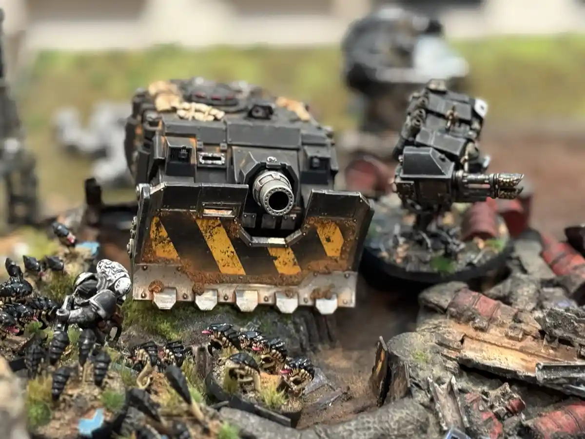 A close-up photo of a heavily detailed, painted Warhammer 40k tank miniature with yellow and black hazard stripes on its…