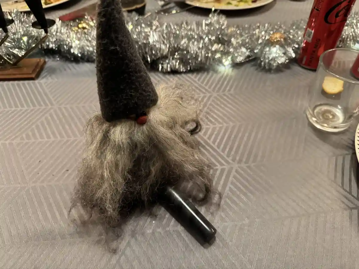 A close-up photo shows a small, handmade gnome figurine with a gray woolen hat and a long, shaggy gray beard, sitting on a…