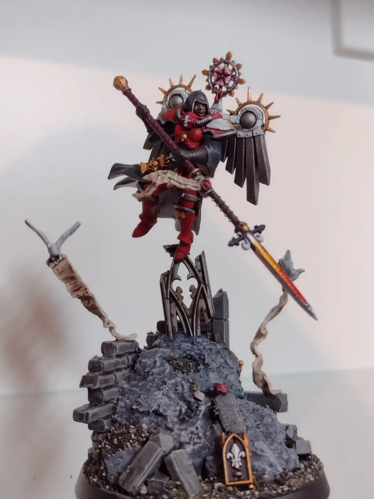A highly detailed, painted miniature of a red-armored fantasy warrior with a hood, wielding multiple weapons including a…