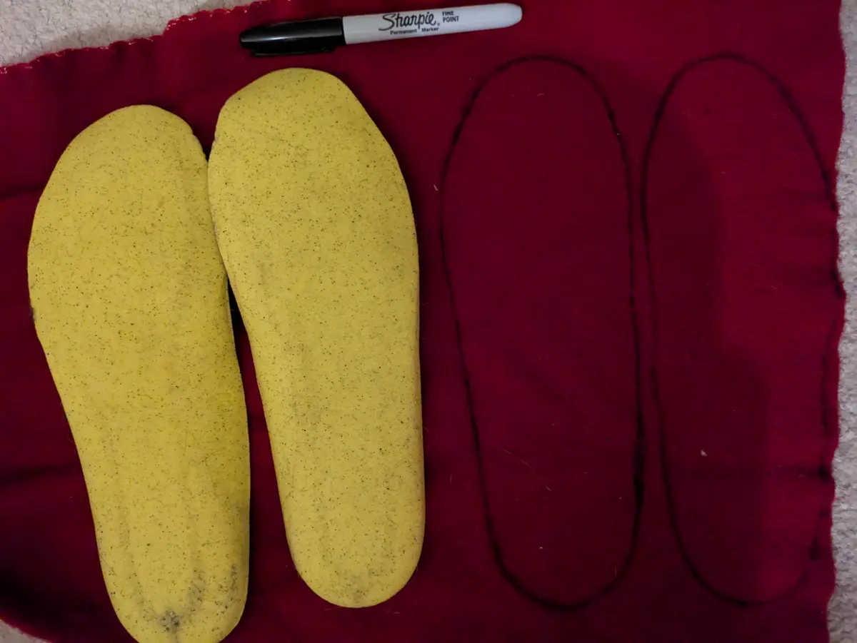 A photo shows two yellow, speckled insoles placed next to two identical outlines traced on a red felt mat, with a black…