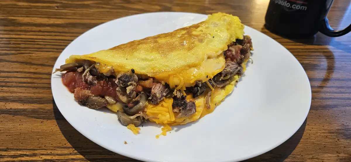 A close-up photo shows a folded, golden-brown omelette on a white plate, revealing a filling of shredded meat, melted…