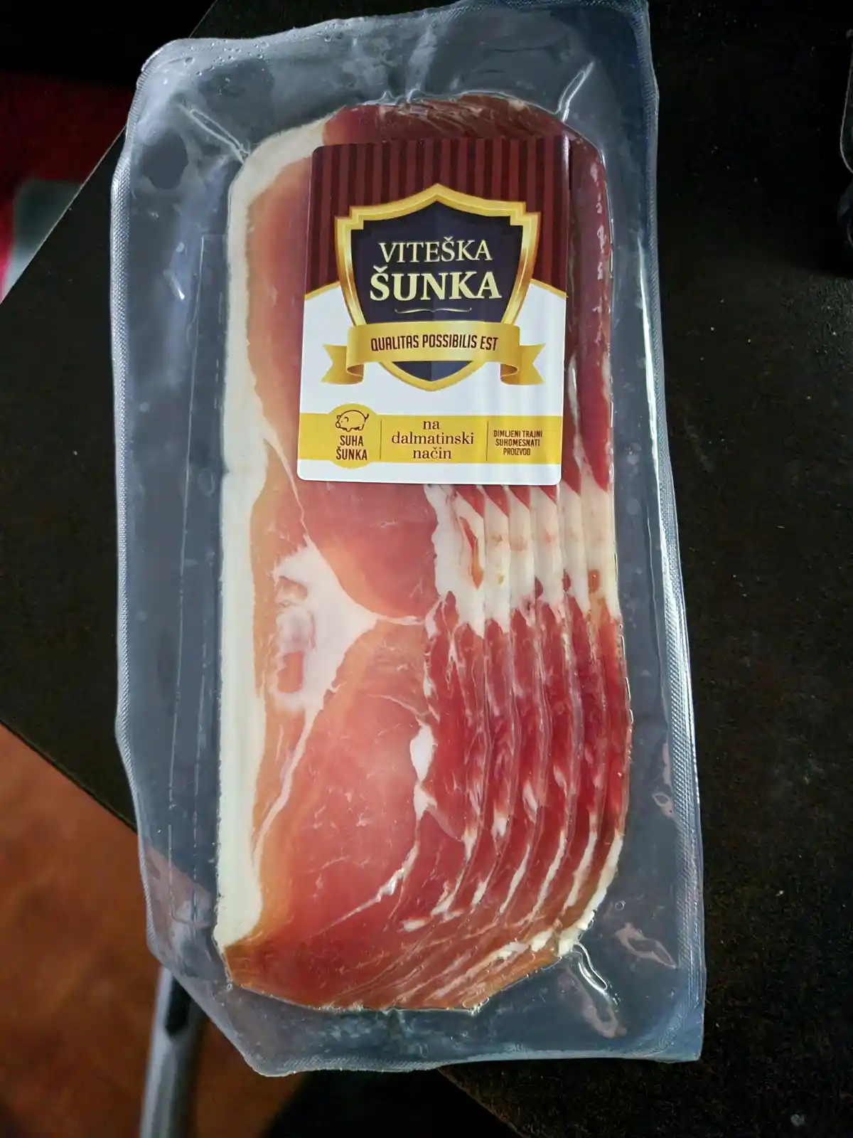 A package of vacuum-sealed cured ham labeled 'Viteška Šunka' with Latin phrase 'Qualitas Possibilis Est' and Croatian text…