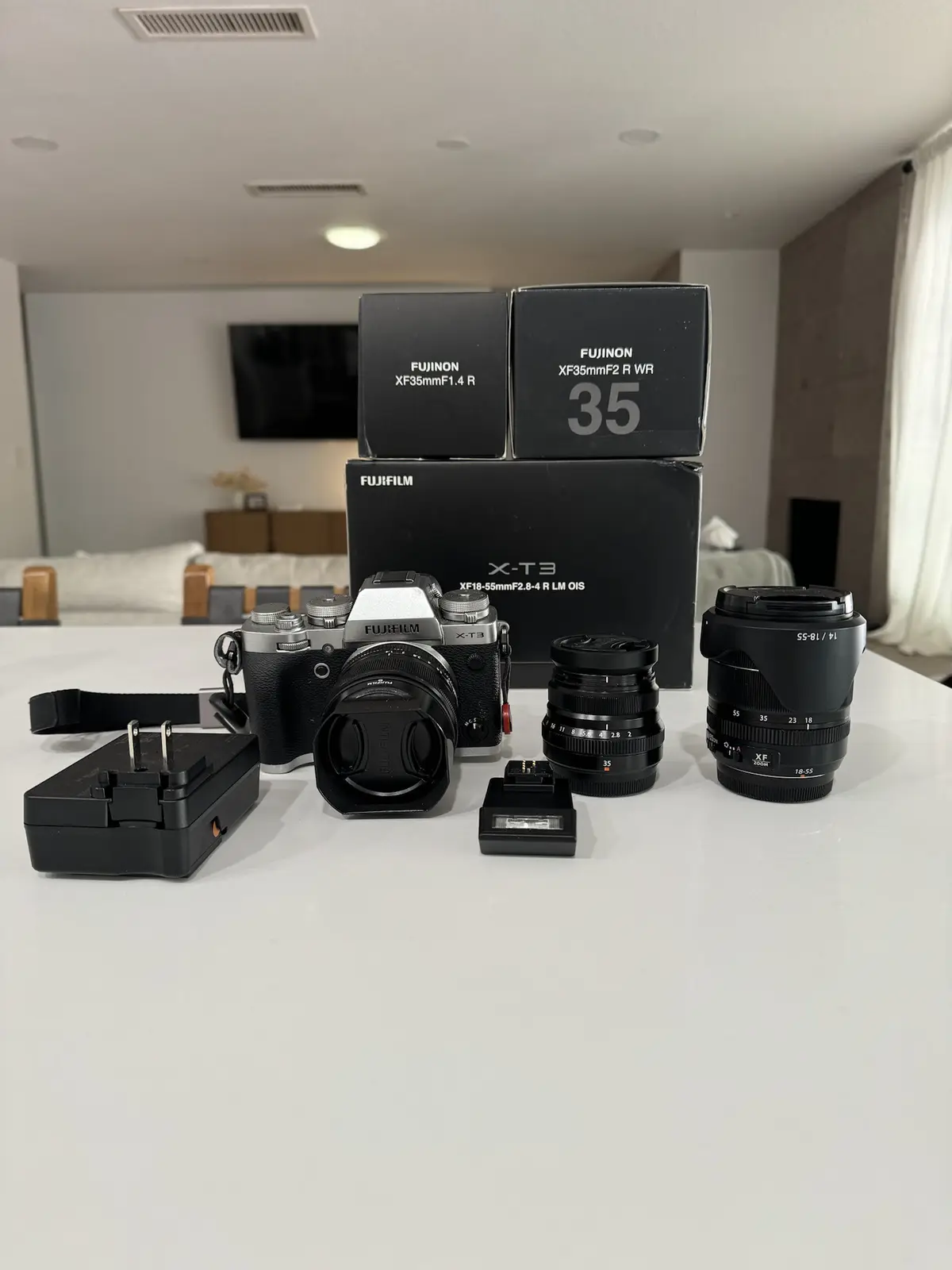 A Fujifilm X-T3 camera and its accessories are displayed on a white table, including two lens boxes (XF35mmF1.4 R and…