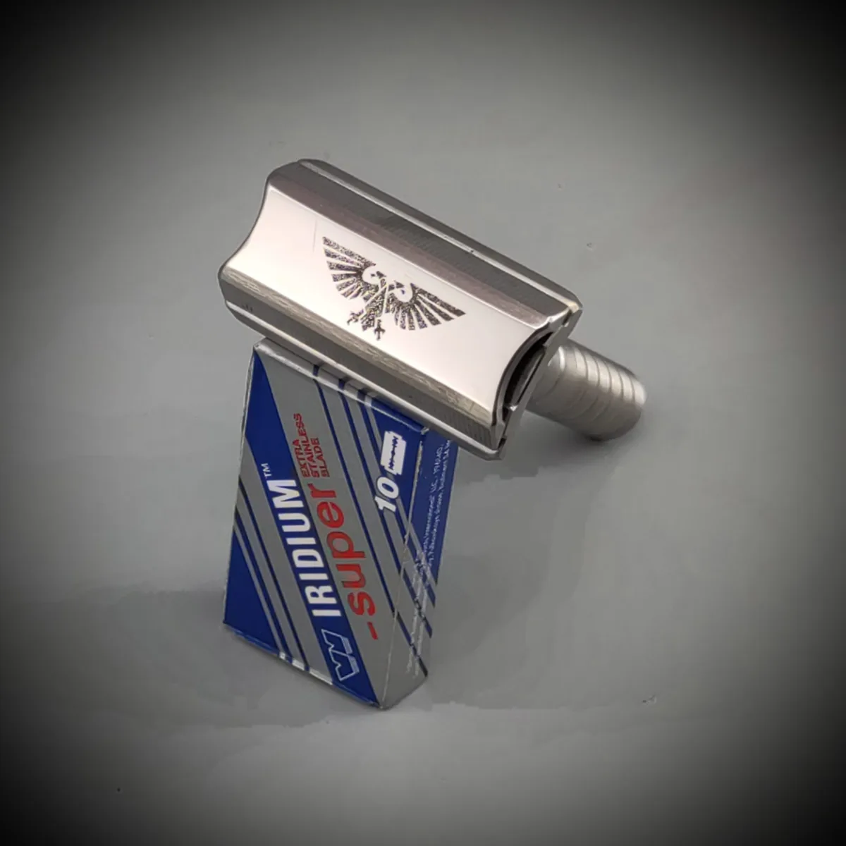 A silver safety razor with an eagle emblem is balanced upright on a blue and silver box labeled 'IRIDIUM super 10' which…