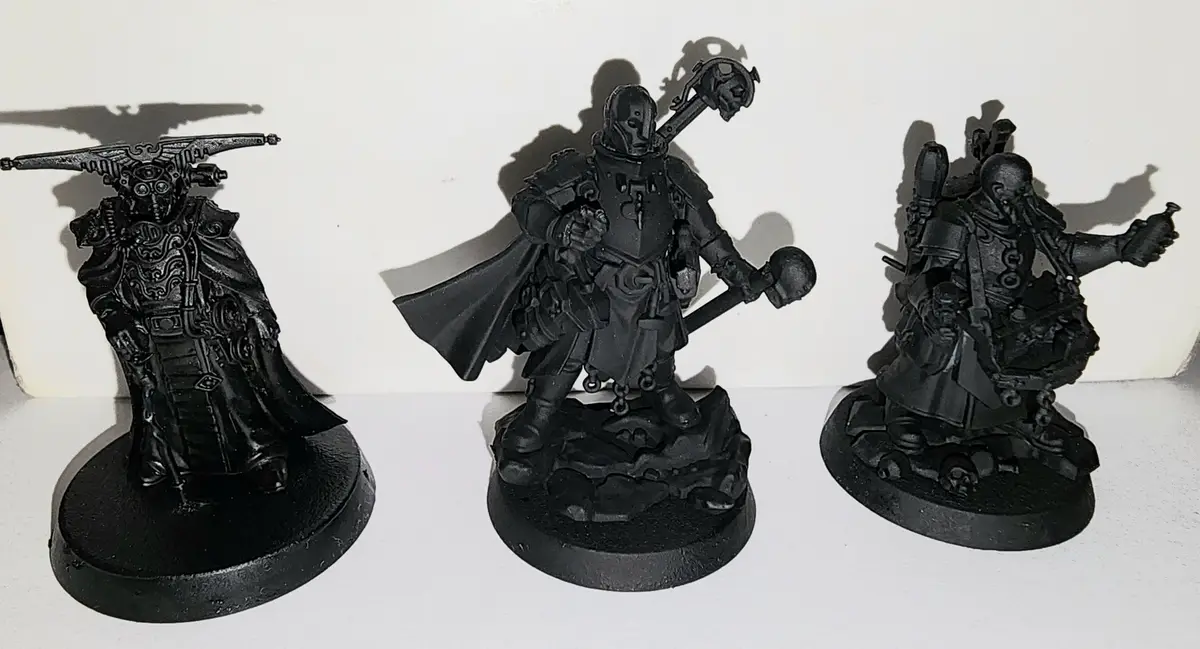 Three black-painted fantasy miniatures stand side-by-side on circular bases against a white background. The left figure…