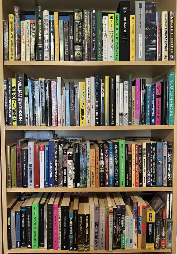 A bookshelf filled with numerous editions of William Gibson's 'Neuromancer' in various languages and cover designs, all…