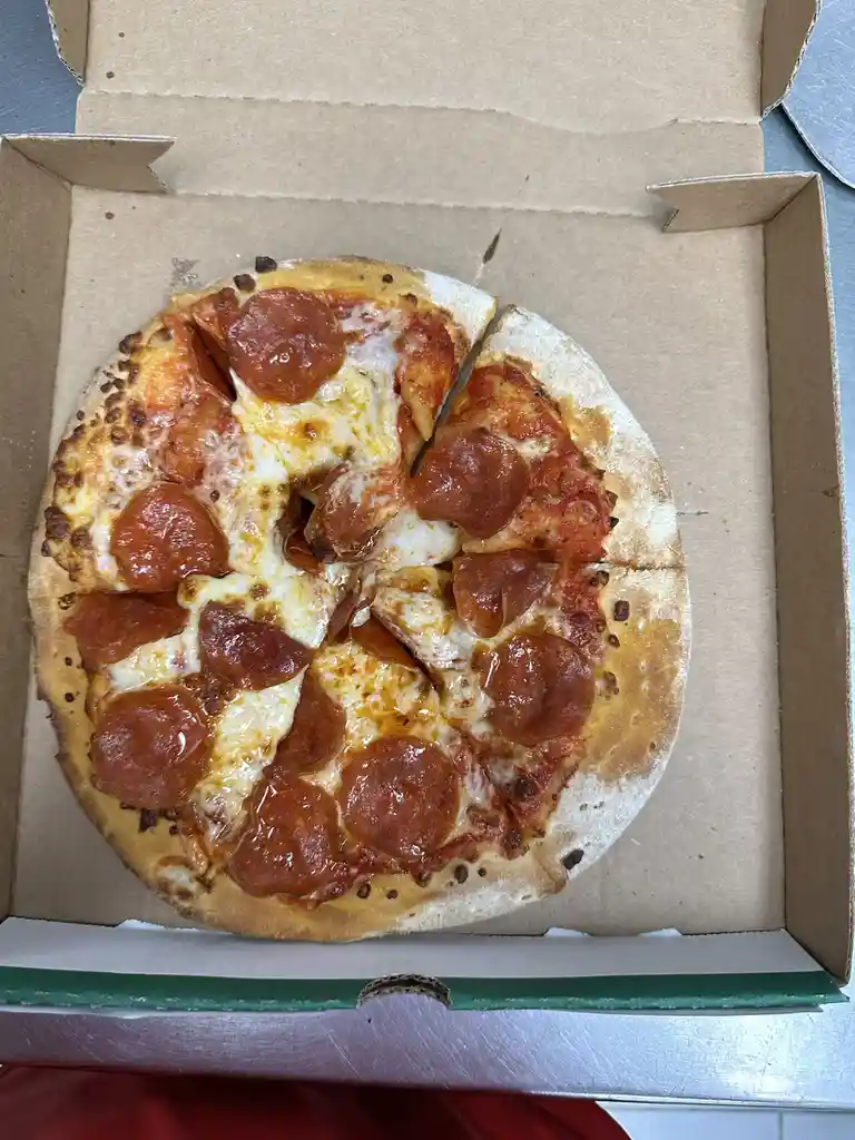 A top-down photo shows a pepperoni pizza in an open cardboard box, with one slice visibly missing, revealing the box's…