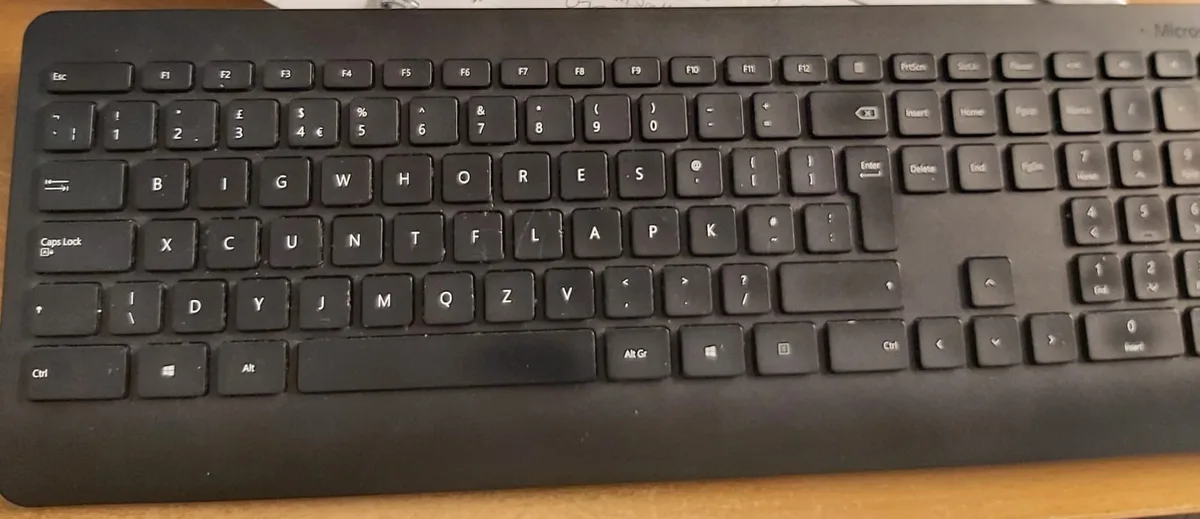 A black computer keyboard with the letters on the main QWERTY keys altered to spell 'BIG WHORES COUNT LA P K' in all caps…