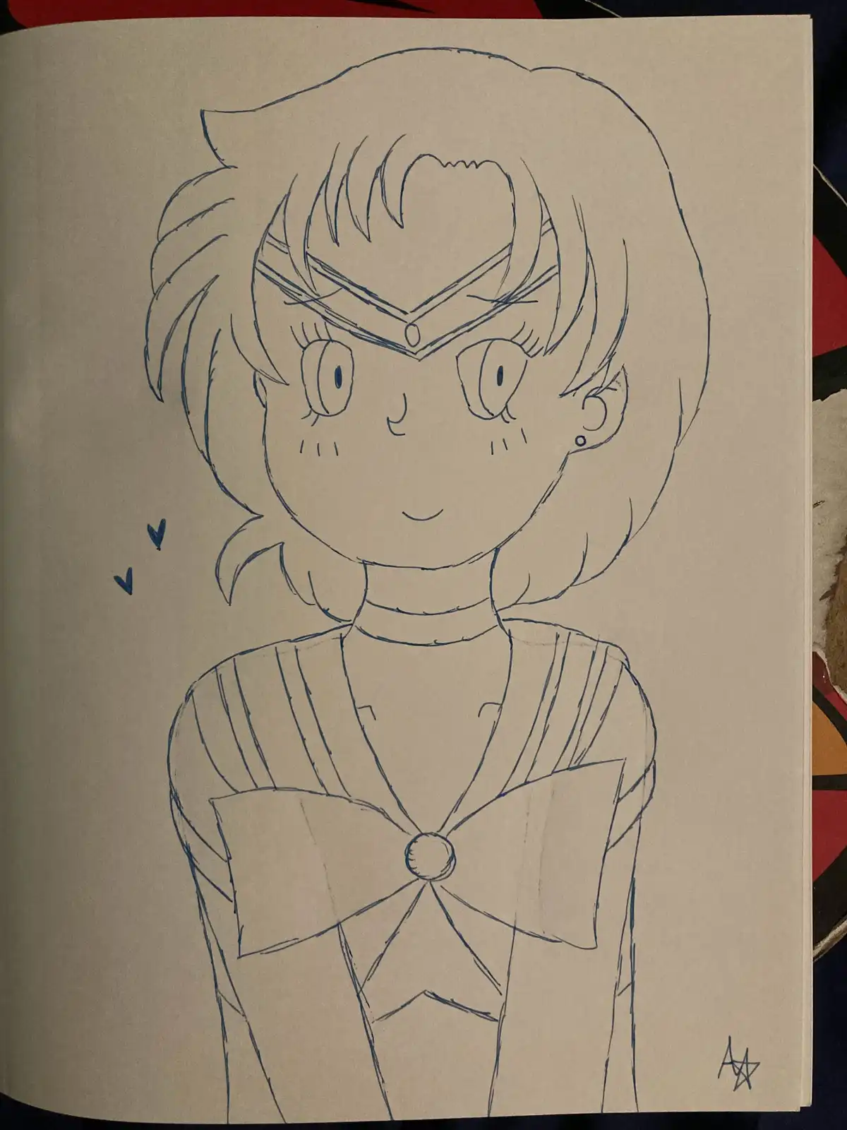 A hand-drawn blue ink sketch on beige paper depicts an anime-style girl with short hair, a headband, and a sailor uniform…