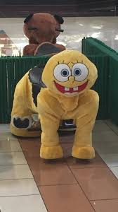 A yellow plush mascot resembling SpongeBob SquarePants is shown in a crouching position on a tiled floor, with a large brown…