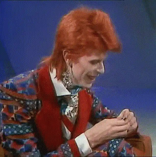 six panels show David Bowie in a colorful patterned suit with red vest and orange hair, smiling and laughing while seated…