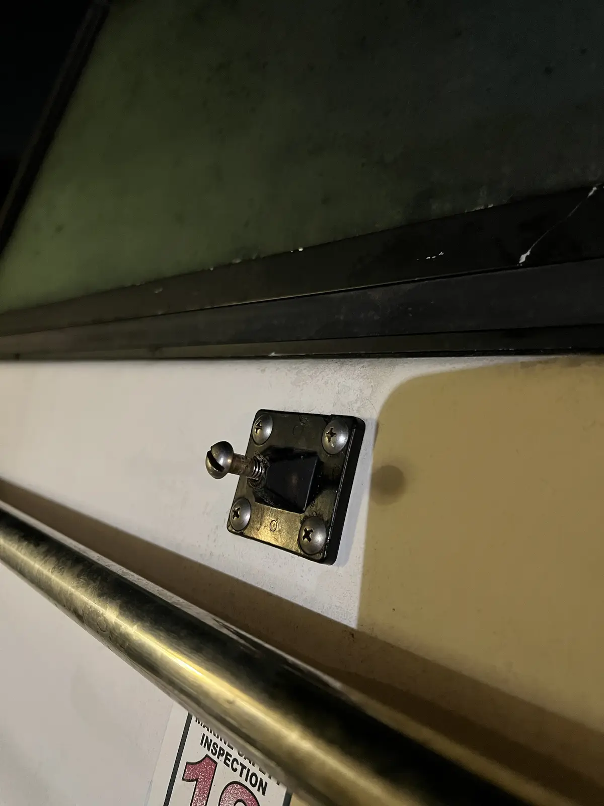 A close-up photo shows a metal toggle switch mounted on a boat's white hull, secured with four screws. Below it, a portion…