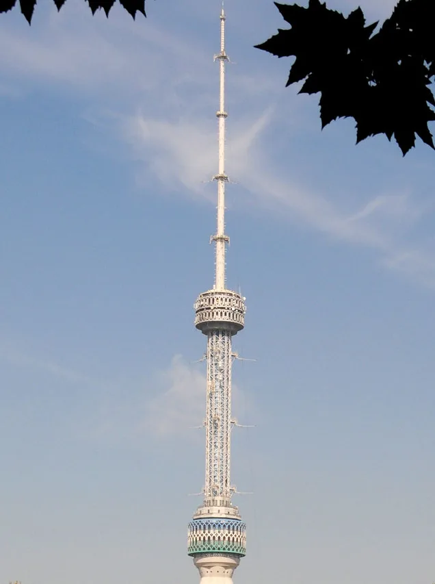A tall, slender white telecommunications tower with a decorative lattice structure and antenna array stands against a clear…