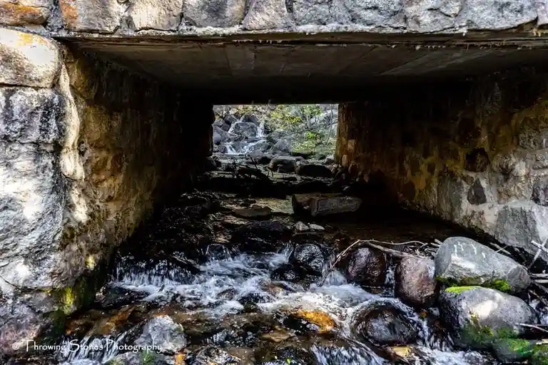 A photo taken from under a stone bridge looking upstream at a rocky stream. The overlaid text reads 'i'm not a fan of the…