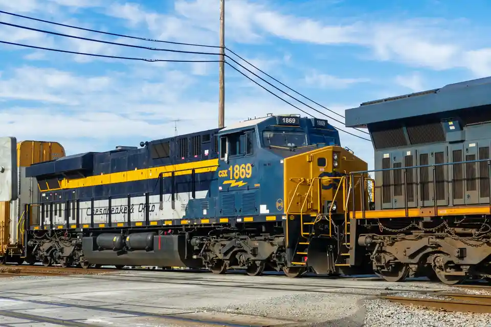 A blue and yellow CSX locomotive numbered 1869 is shown on train tracks under a partly cloudy sky, with the text 'csx 1869'…
