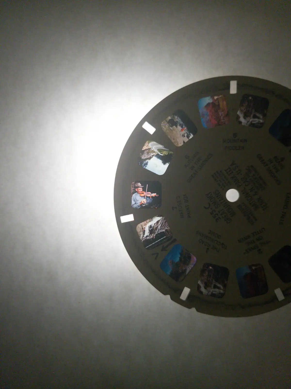 A close-up photo of a vintage View-Master reel, showing its circular cardboard disc with multiple small square images of…