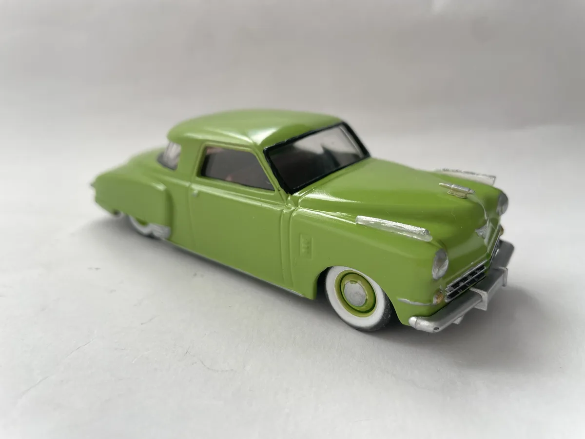 A lime green vintage-style toy car with white wall tires and chrome accents is photographed on a plain white surface. The…
