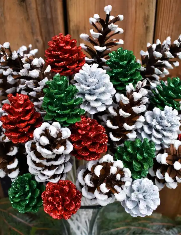 A close-up of a festive bouquet made of pinecones painted in red, green, and white glitter, with artificial snow dusted on…
