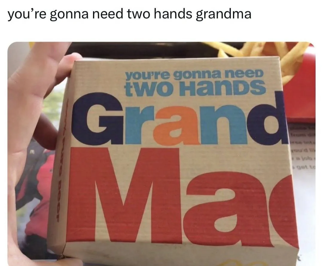 A hand holds a McDonald's Grand Mac box, which has the text 'you're gonna need two hands' printed on it. The same phrase is…