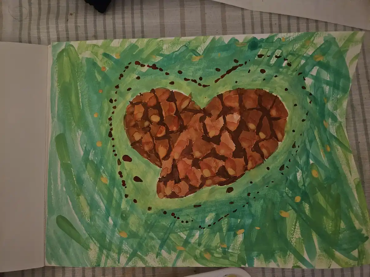 A child's watercolor painting shows a heart-shaped waffle with brown grill marks and yellow dots, set against a green grassy…