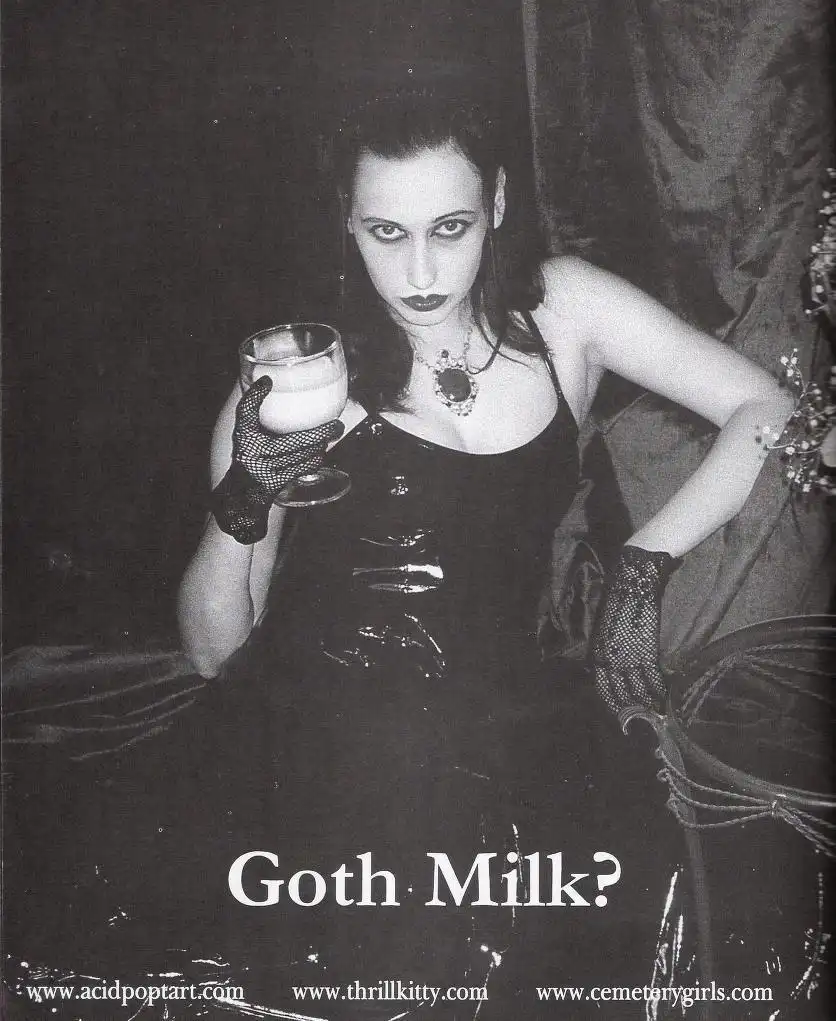 A black-and-white photo of a woman in goth attire, including dark lipstick, fishnet gloves, and a black dress, holding a…