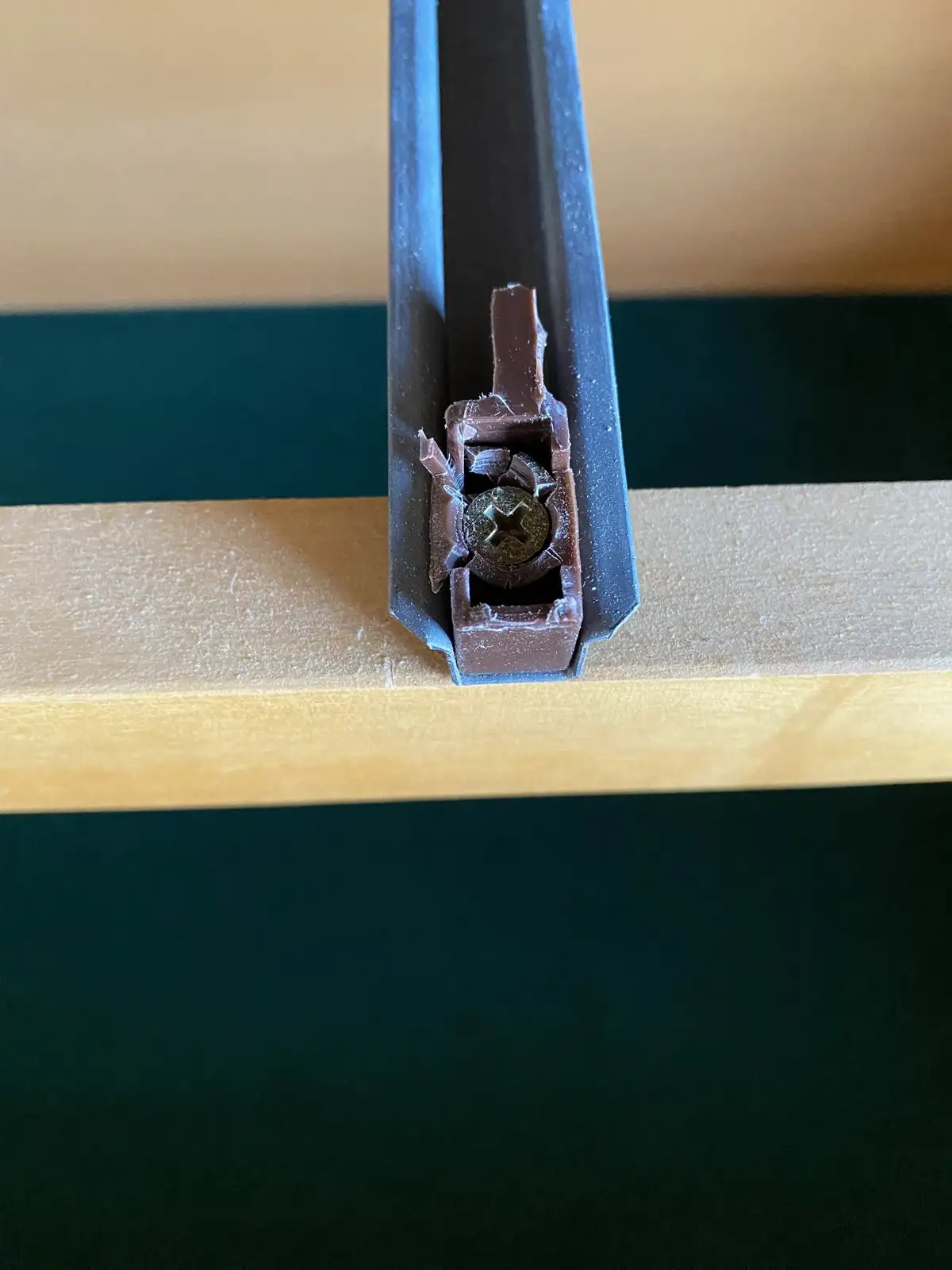 A close-up photo shows a broken brown plastic hinge or latch mechanism, with a visible screw in the center, embedded in a…