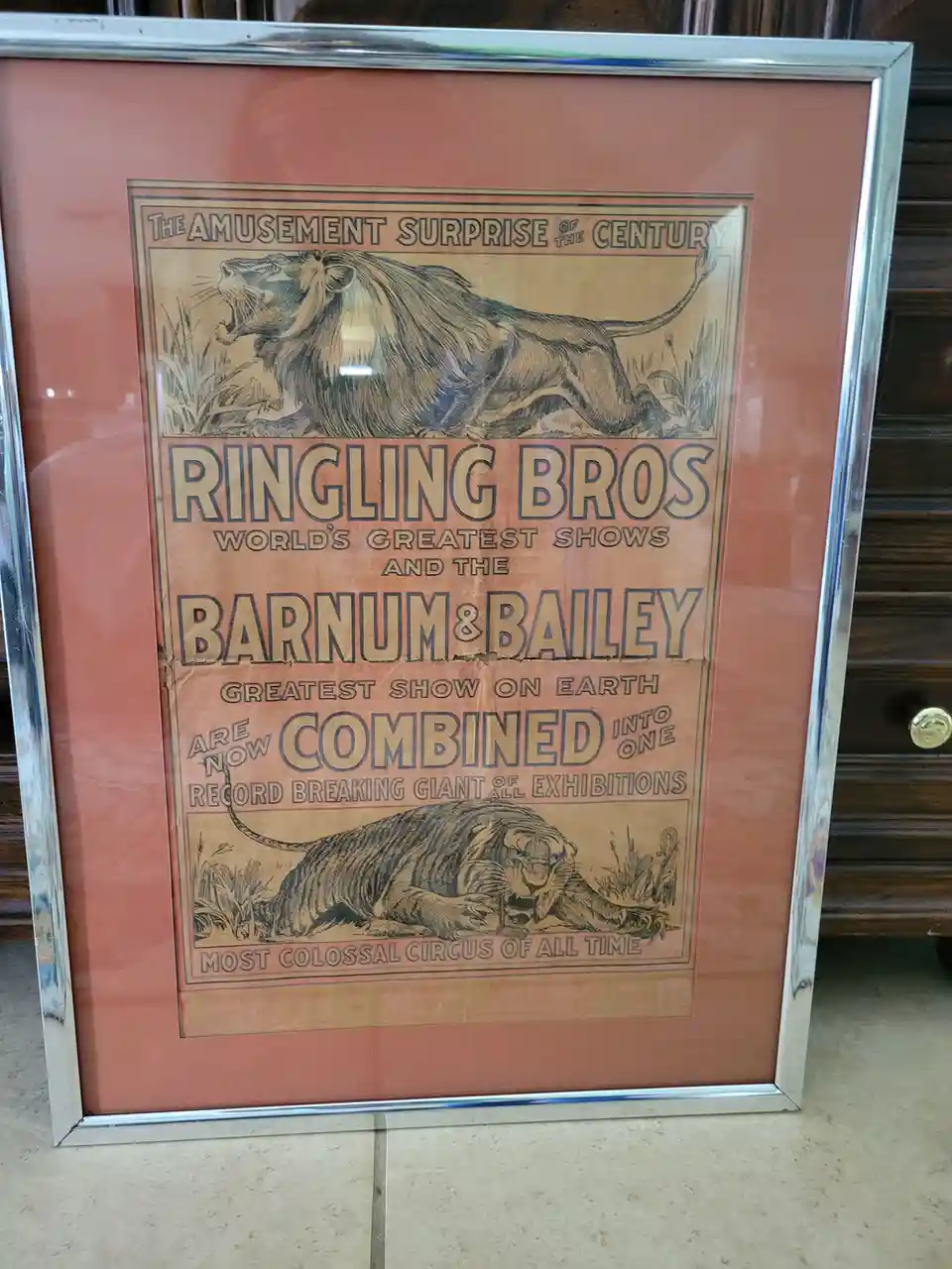 A vintage Ringling Bros and Barnum & Bailey circus poster, framed and displayed indoors, features illustrations of a roaring…