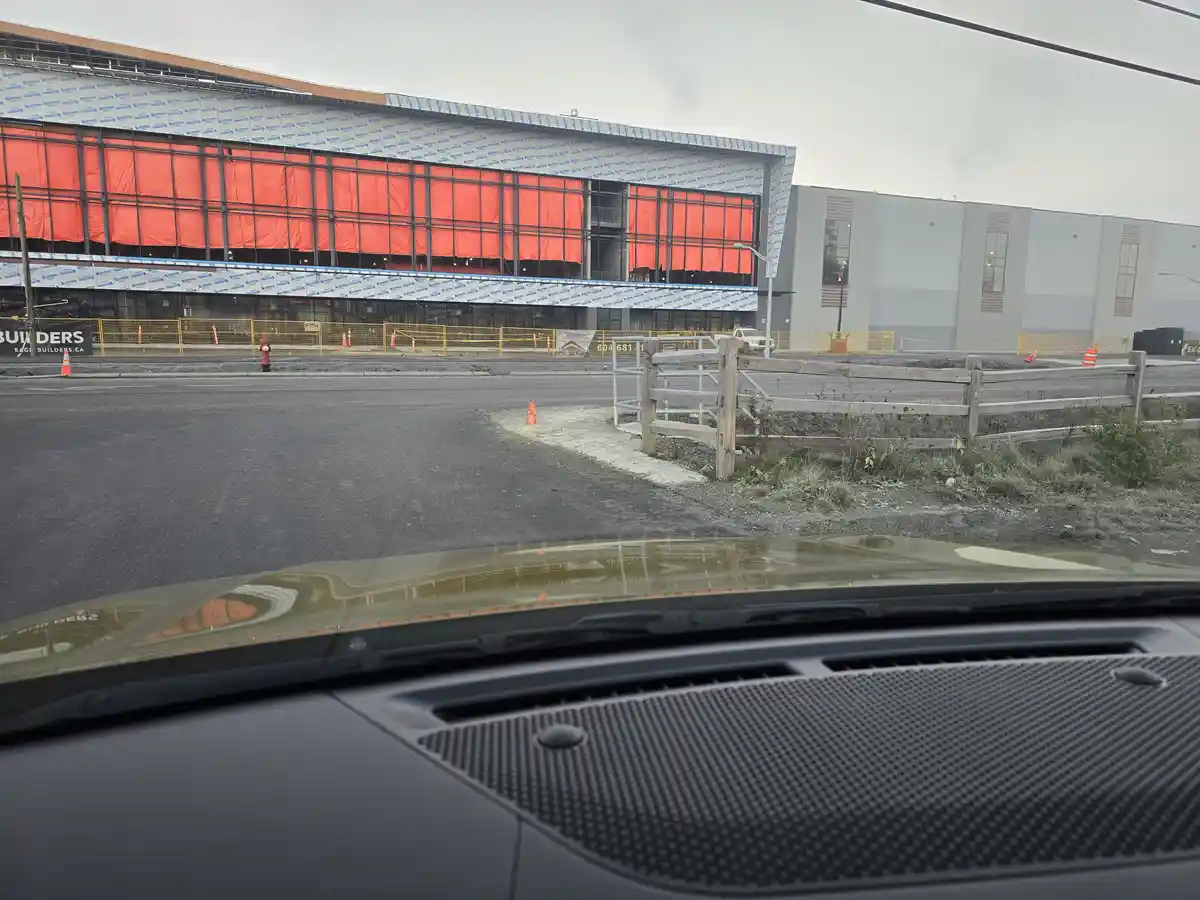 A photo taken from inside a car shows a large building under construction with red tarps covering windows and blue…