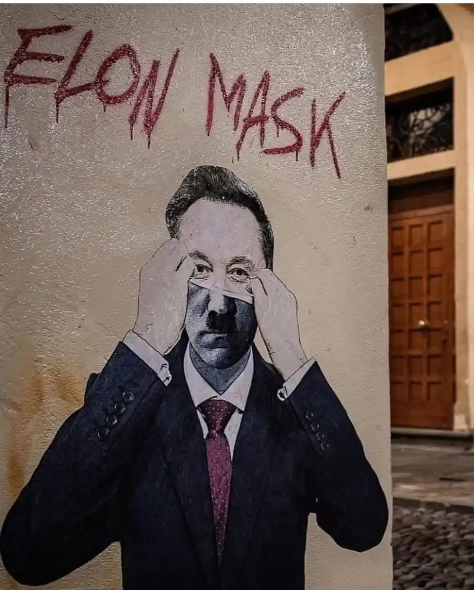 A street mural depicts a man in a suit and tie, holding a white strip across his eyes as if wearing a mask. Above him, red…