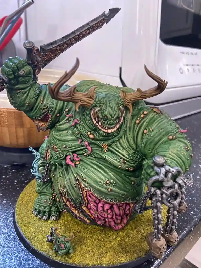 A highly detailed, green, monstrous figurine with horns, wielding a large sword and holding a chain, sits on a kitchen…