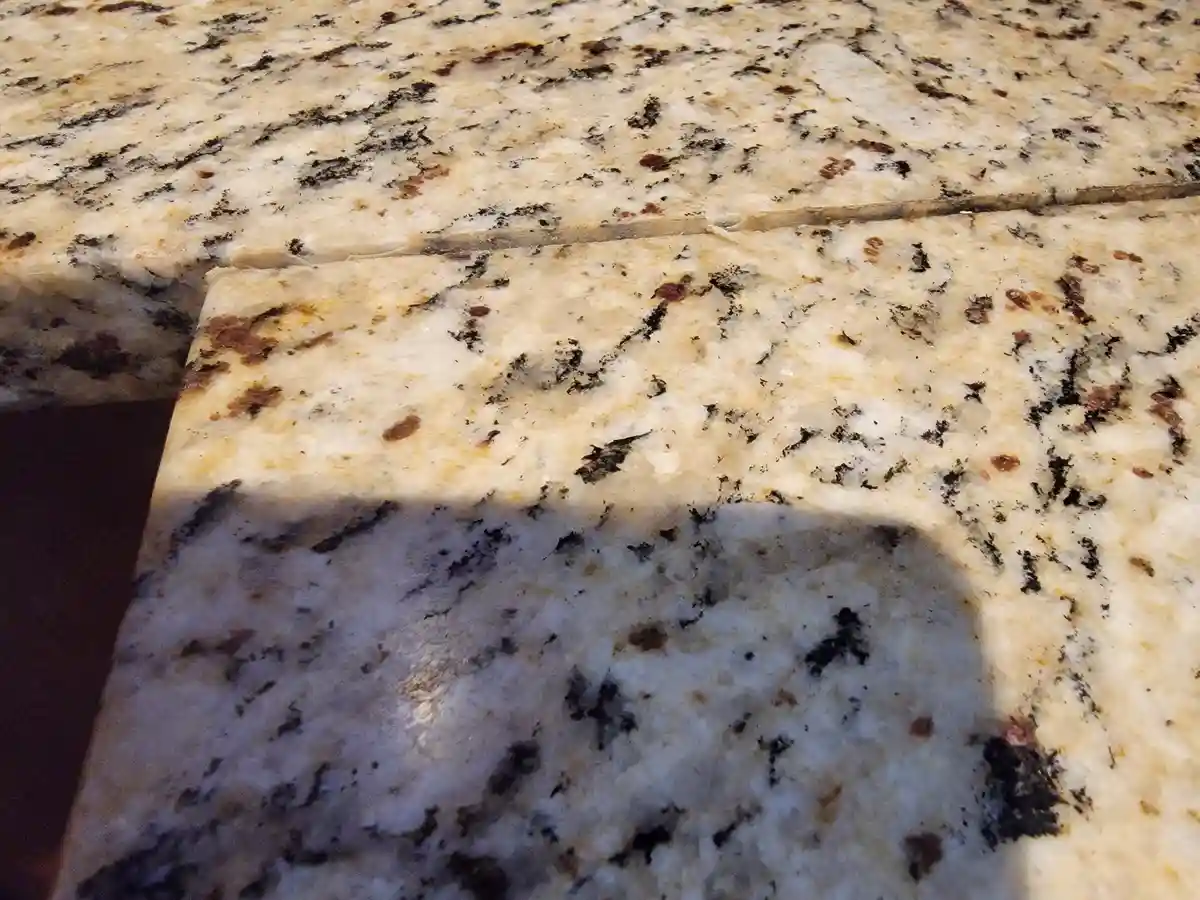 A close-up photo shows a light-colored granite countertop with black and brown speckles, featuring a visible crack running…
