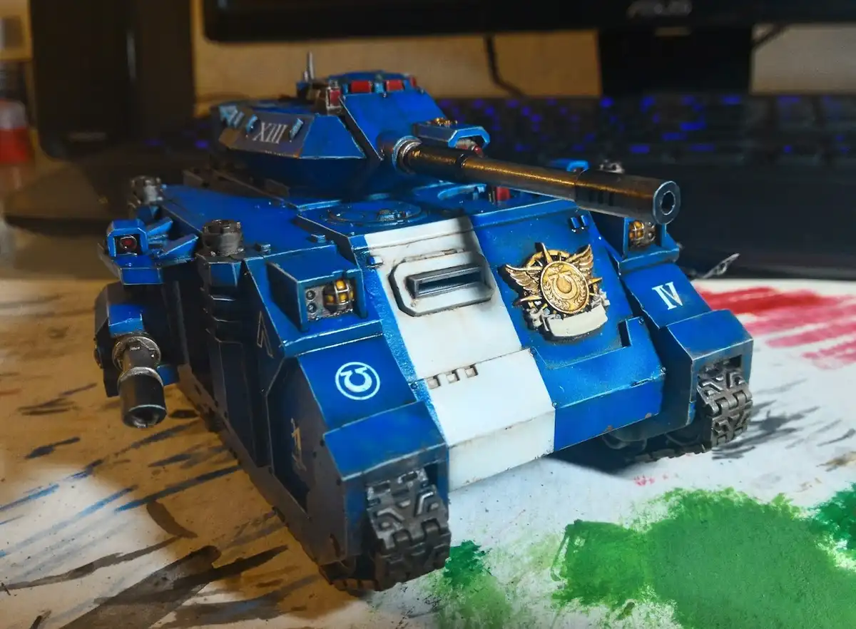 A detailed blue and white painted model of a Warhammer 40,000 tank sits on a paint-splattered work surface, with Roman…