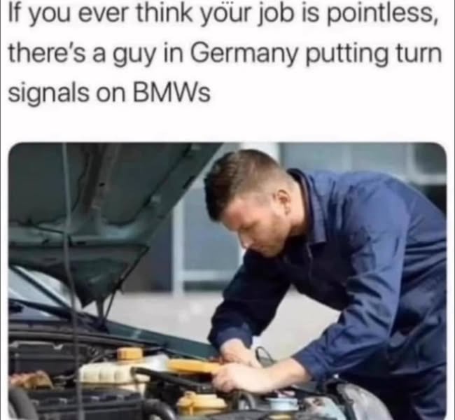 A man in a blue work uniform is bent over the open hood of a car, appearing to work on the engine. The overlaid text reads…